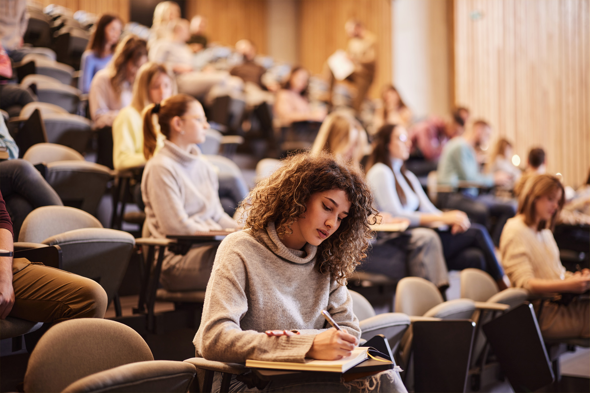 a woman sits in a lecture hall writing in a notebook